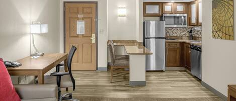A compact hotel room with a kitchenette, a dining area with a table and chairs, and a small seating area with a sofa.