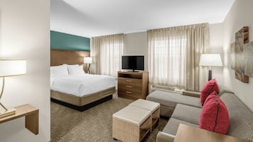 A hotel room with a bed, a desk, a television, a sofa, and a window with curtains.