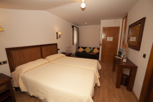 A hotel room with a double bed, bedside tables, a mirror, and a small table with a vase.