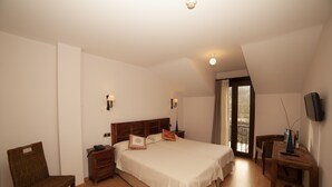 Un dormitorio con una cama grande, cabecera de madera, mesitas de noche, una silla, un televisor y una ventana con vistas.