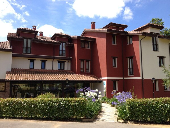 A multi-story building with a red and white facade, a tiled roof, and a garden with various plants and flowers.