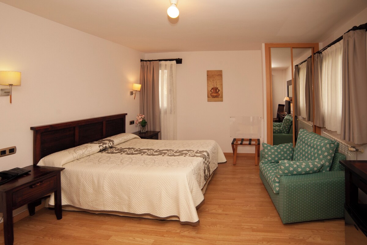 Habitación de hotel con dos camas, un escritorio, una mesita pequeña, un sofá y un espejo.