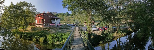 Un hotel a la orilla del río con un puente, terraza al aire libre y vistas del río.