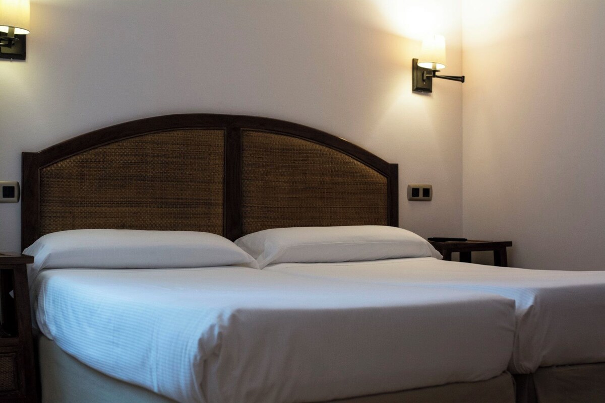A neatly made bed with a wooden headboard, two bedside tables, and wall-mounted lights.