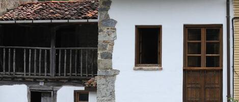 Un edificio de piedra tradicional con techo de tejas, un balcón de madera y un pequeño jardín.