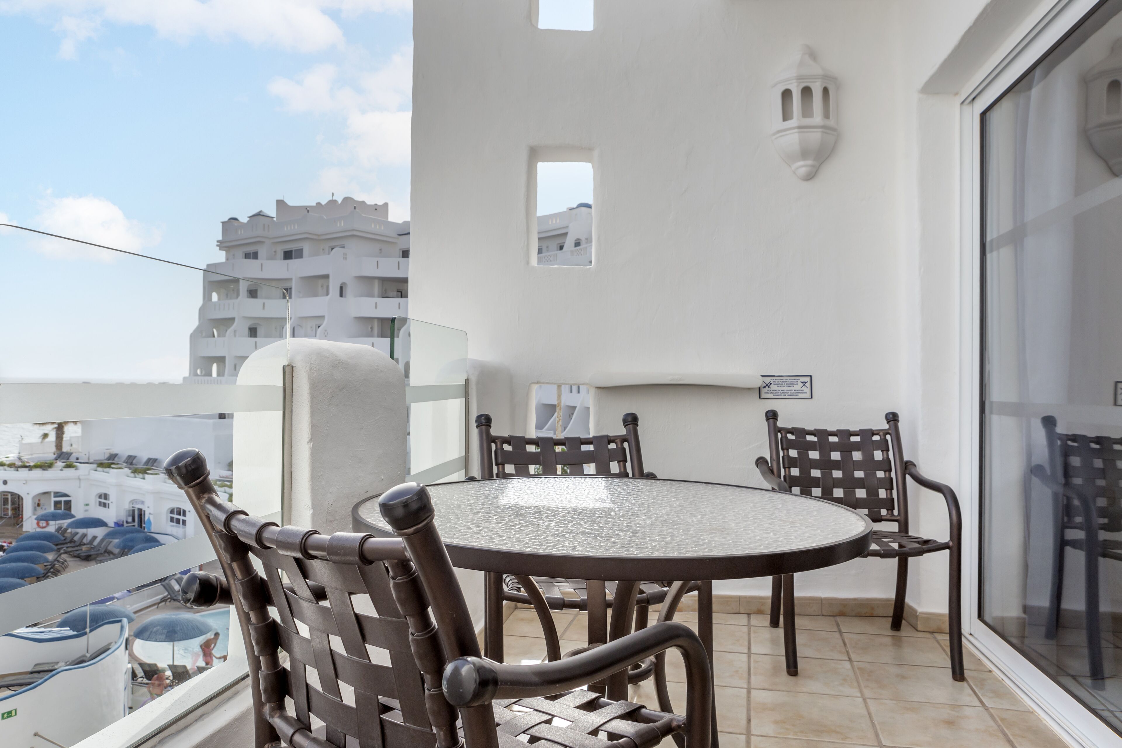 Een balkon met een ronde tafel en vier stoelen, met uitzicht op een stadsbeeld.