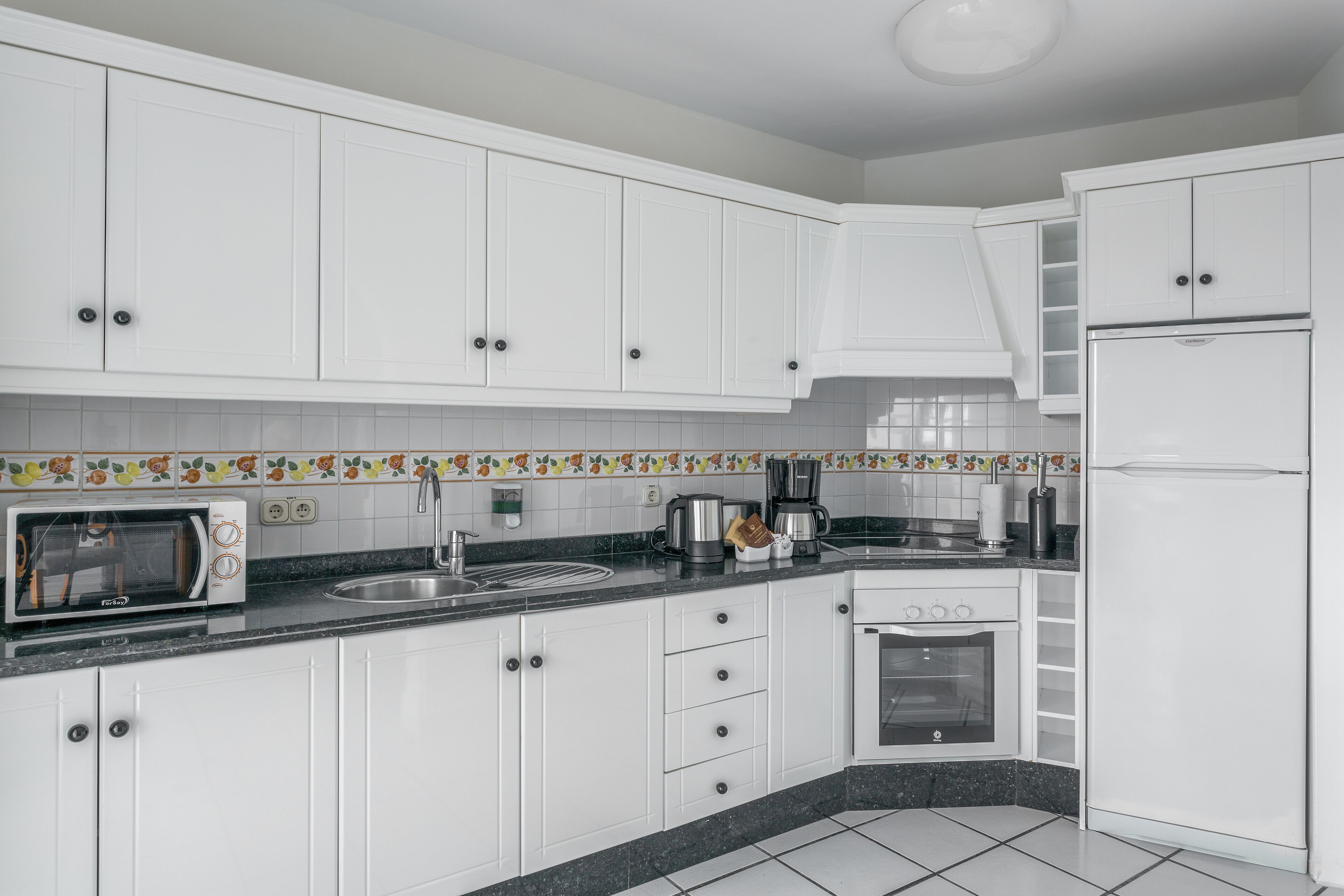 A kitchen with white cabinets, a microwave, a coffee maker, and a refrigerator.