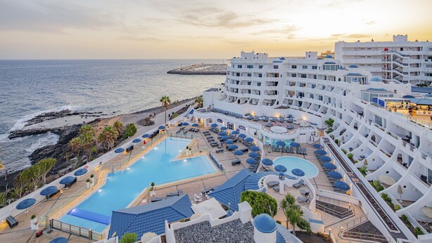 Un complexe hôtelier doté d’une grande piscine, de chaises longues et offrant une vue sur la mer.