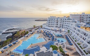 Un complexe hôtelier doté d’une grande piscine, de chaises longues et offrant une vue sur la mer.