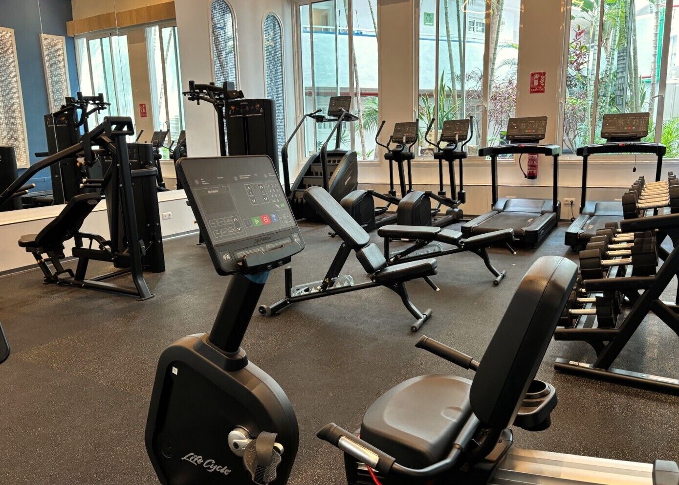 Un gimnasio con máquinas de cardio, bancos de pesas y mancuernas.