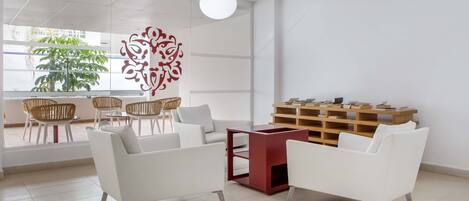 A modern, well-lit office space with white furniture, a red accent table, and a decorative wall piece.