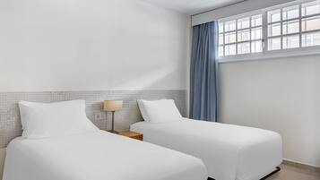 Una habitación de hotel con dos camas, una mesita de noche, una lámpara y una ventana con cortinas.
