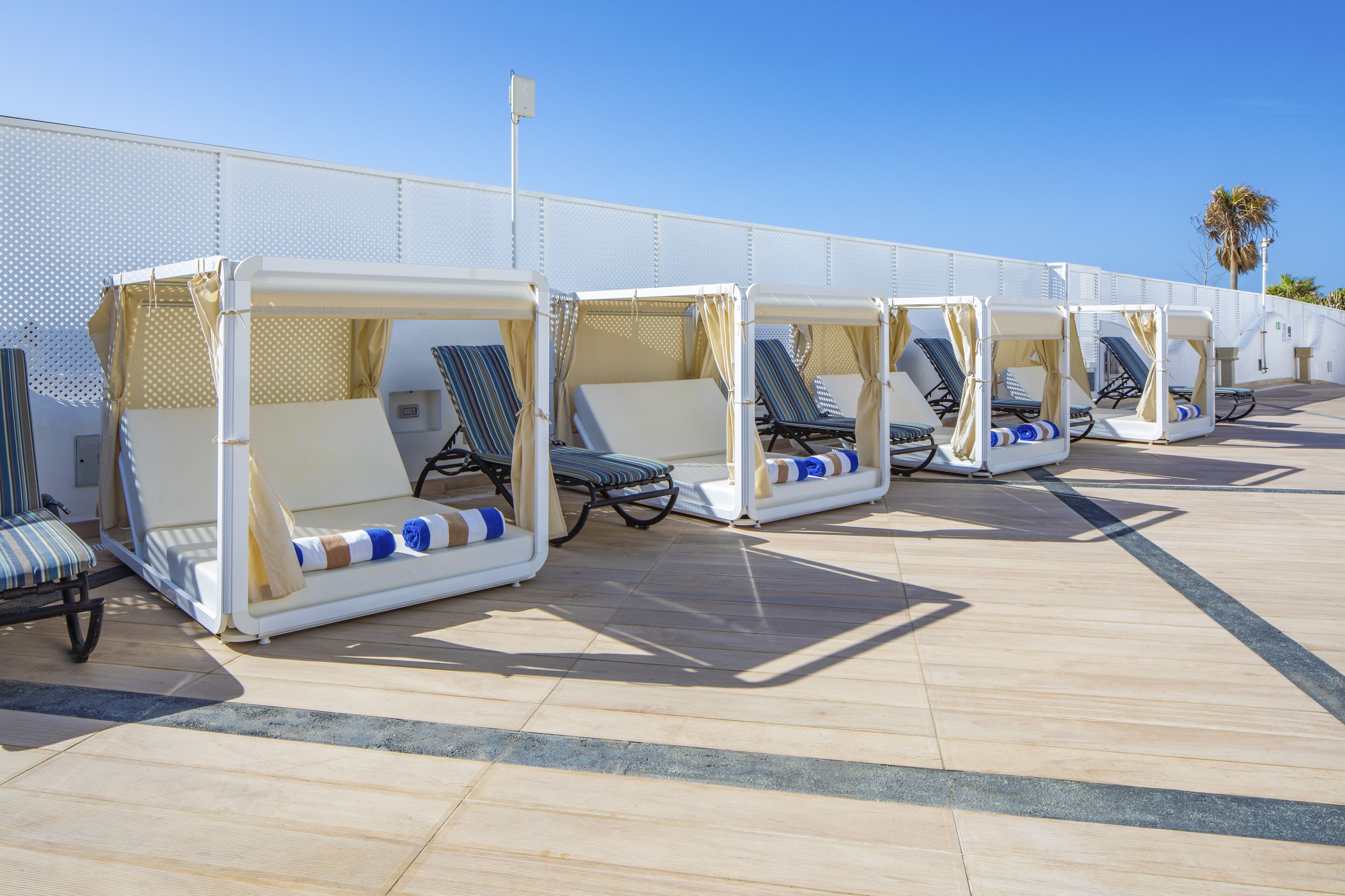 A row of sun loungers with canopies, arranged on a tiled deck.