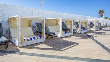 A row of sun loungers with canopies, arranged on a tiled deck.