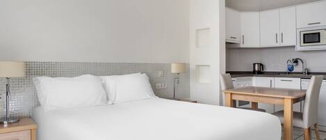 A hotel room with a bed, bedside tables, a desk, and a kitchenette.