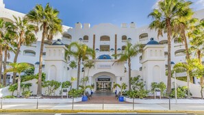Un grand bâtiment blanc, doté d’un dôme central et de nombreux balcons, entouré de palmiers.