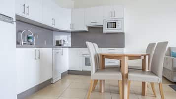 Een moderne keuken met witte kasten, een magnetron, een waterkoker en een eettafel met stoelen.