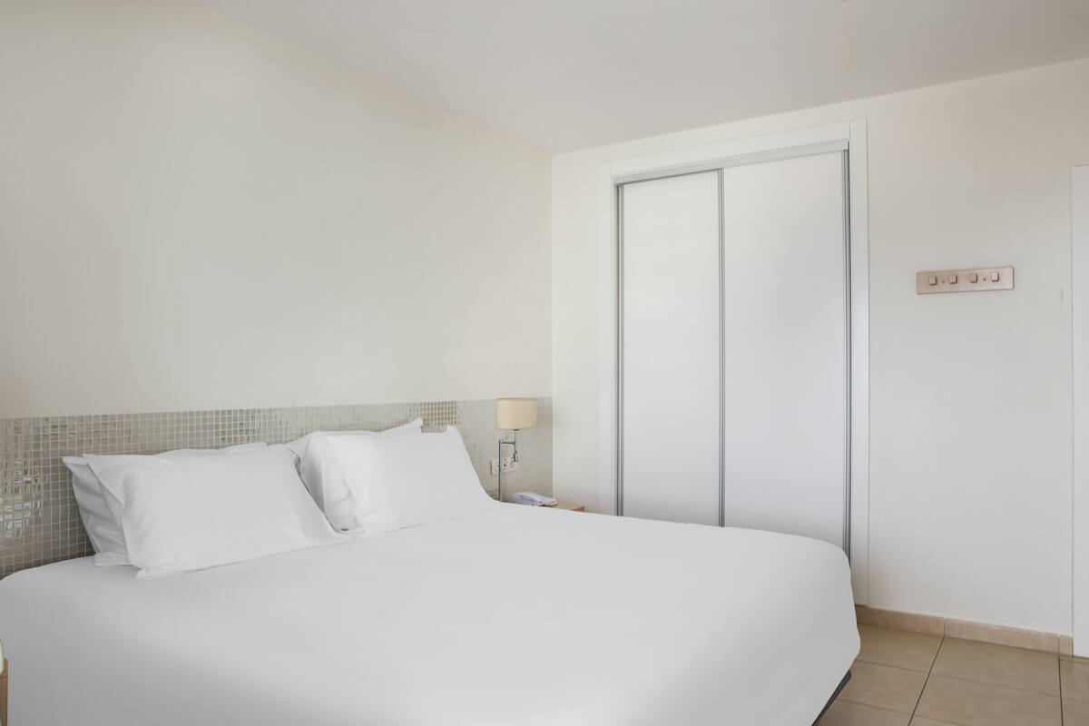 Une chambre d’hôtel comprenant un lit, une table de chevet, une lampe, une armoire et un interrupteur fixé au mur.