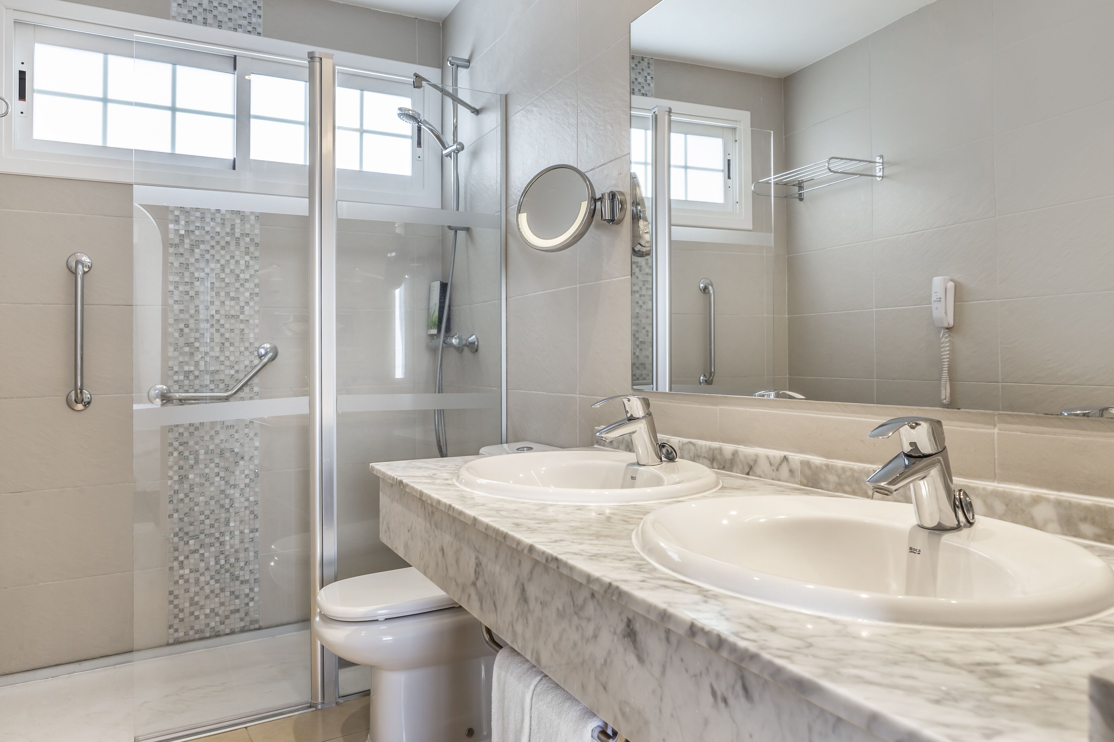A modern bathroom with two sinks, a glass shower enclosure, and a large mirror.