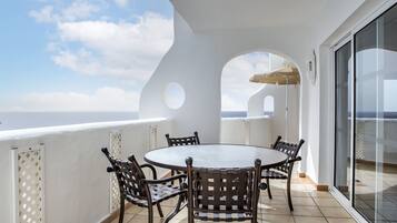 A balcony with a round table and chairs, a glass door, and a view of the sea.
