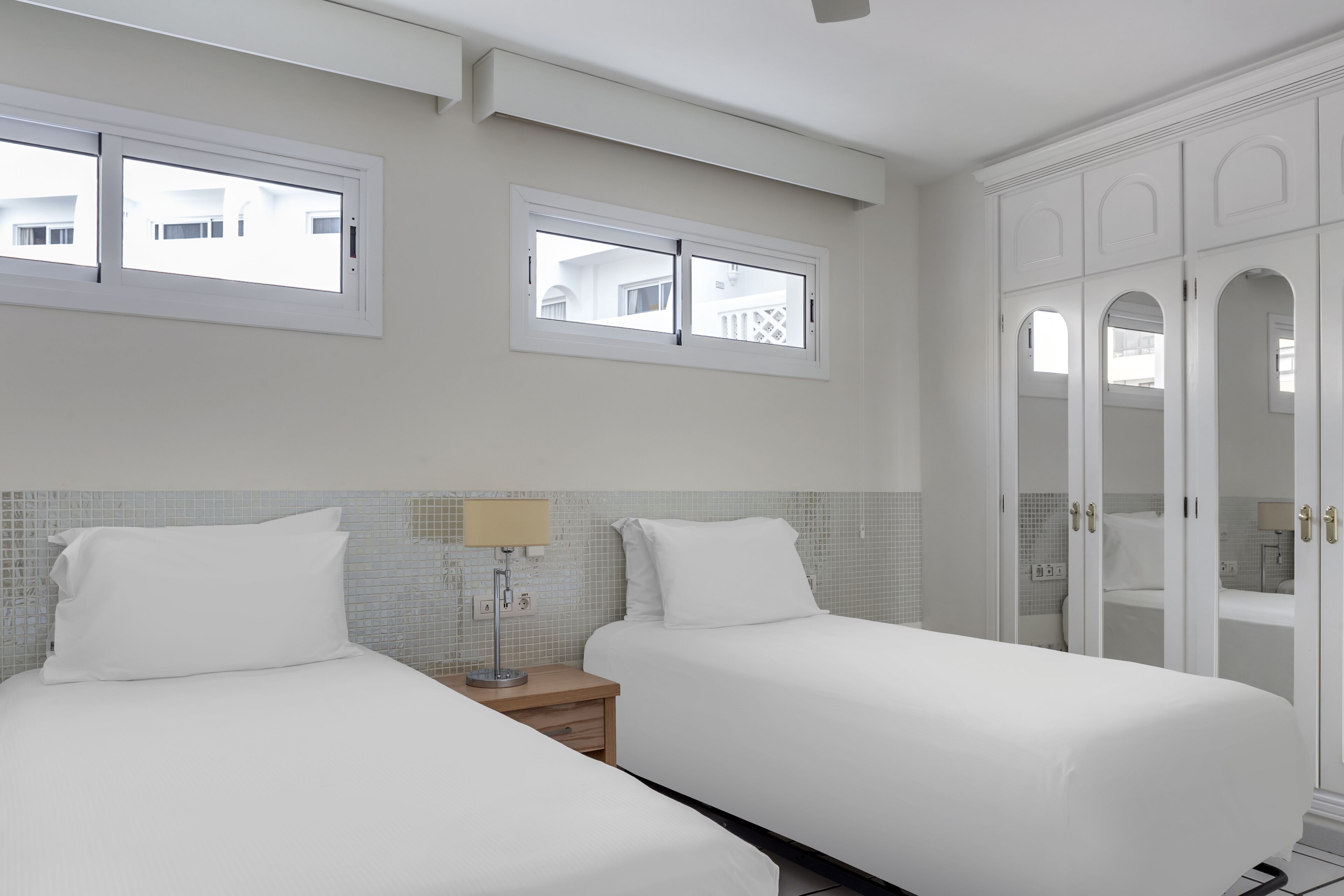 Une chambre d’hôtel avec deux lits, une table de chevet avec une lampe et une armoire avec des portes miroir.