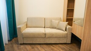 A beige sofa with two cushions in a room with wooden flooring and a wooden wardrobe. - DaunTown Rooms - Self Check-In (Vienna)