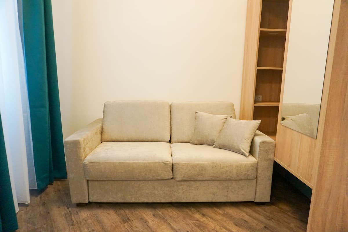 A beige sofa with two cushions in a room with wooden flooring and a wooden wardrobe.