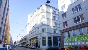A street with parked cars, a tram line, and buildings including a pension and a store with a green sign. - DaunTown Rooms - Self Check-In (Vienna)