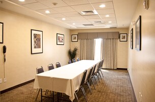 Un salón de conferencias con una larga mesa, sillas, cuadros en las paredes y un ventanal con cortinas.