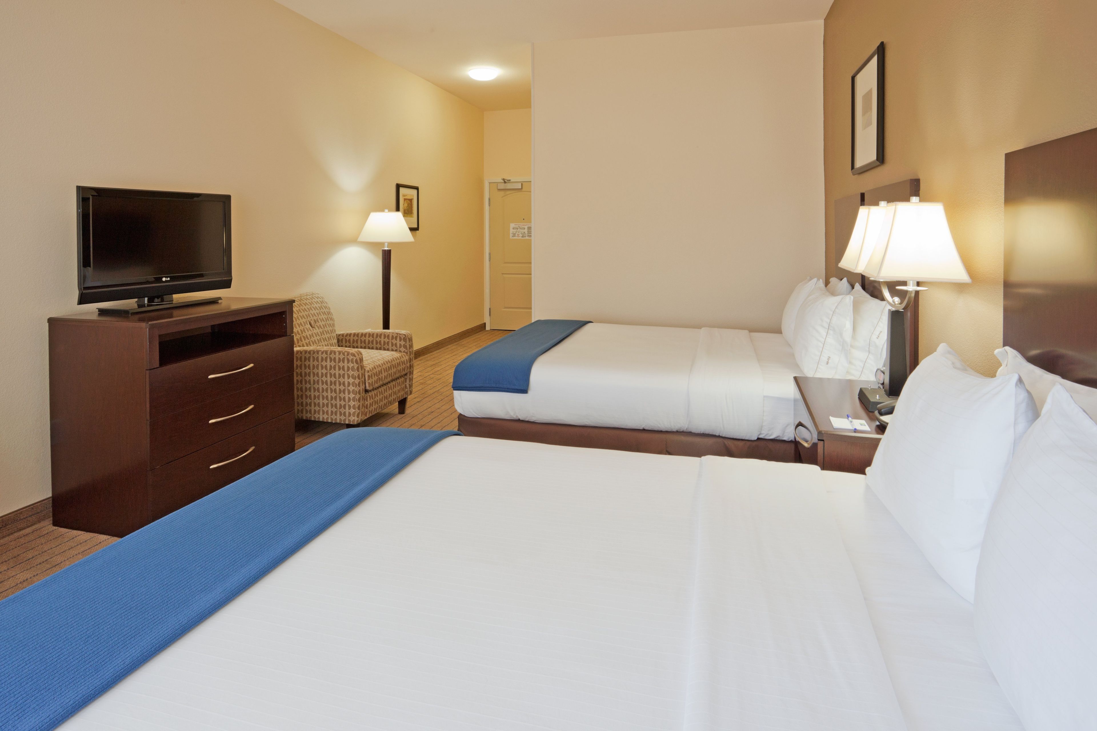 A hotel room with two beds, a TV, a desk, a chair, and a lamp.