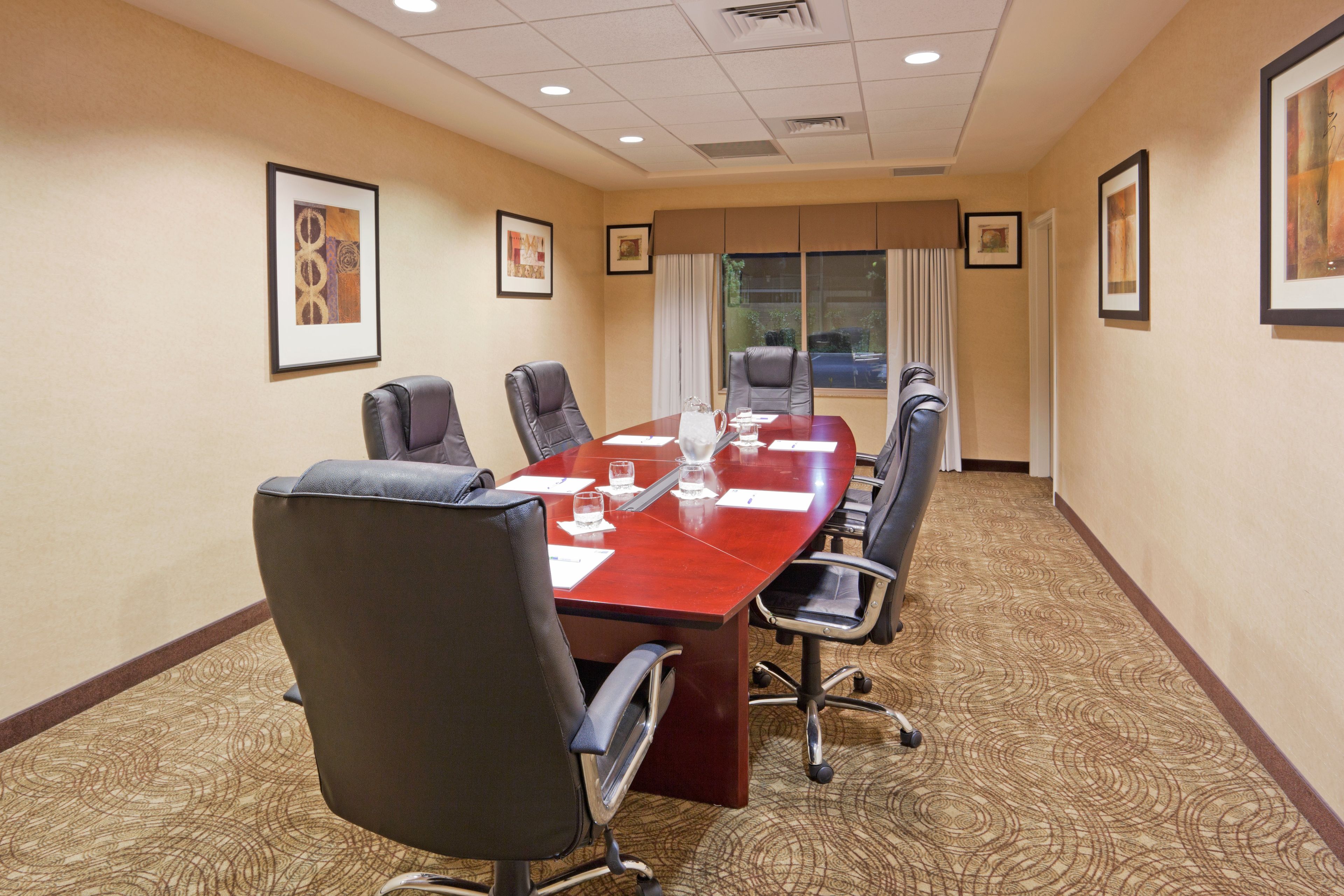 A conference room with a long table, six chairs, and framed artwork on the walls.