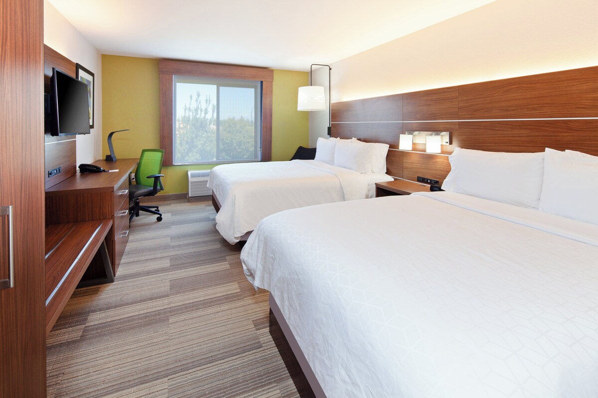 A hotel room with two beds, a desk with a chair, a television, and a window.