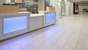 A reception area with a modern design, featuring a reception desk, a wall-mounted information board, and a seating area with a table and chairs. - Holiday Inn Express & Suites Clovis-Fresno Area by IHG (Clovis)