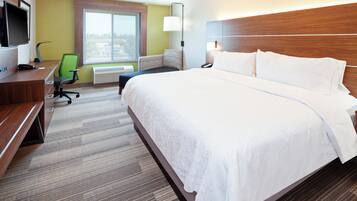 A hotel room with a large bed, a desk with a computer, a chair, a television, and a window with a view.