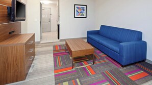 A modern living room with a blue sofa, wooden entertainment unit, and colorful striped carpet. - Holiday Inn Express & Suites Clovis-Fresno Area by IHG (Clovis)