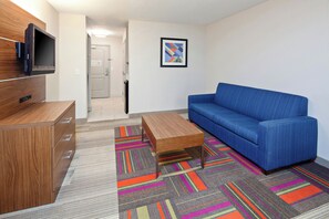 A modern living room with a blue sofa, wooden entertainment unit, and colorful striped carpet. - Holiday Inn Express & Suites Clovis-Fresno Area by IHG (Clovis)