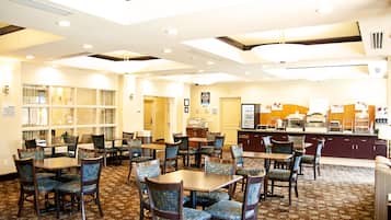 A hotel dining area with multiple tables and chairs, a counter with a menu display, and a patterned carpet.