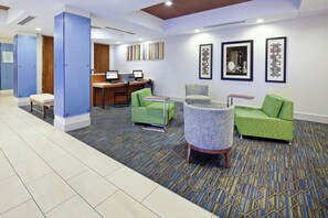 A hotel lobby with a reception desk, two computer stations, a green sofa, a round table, and a patterned carpet.