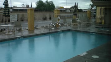 A swimming pool with lounge chairs and umbrellas, surrounded by a fence and a lifeguard warning sign.