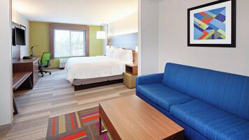 A hotel room with a bed, a blue sofa, a desk with a chair, a television, and a framed picture on the wall.