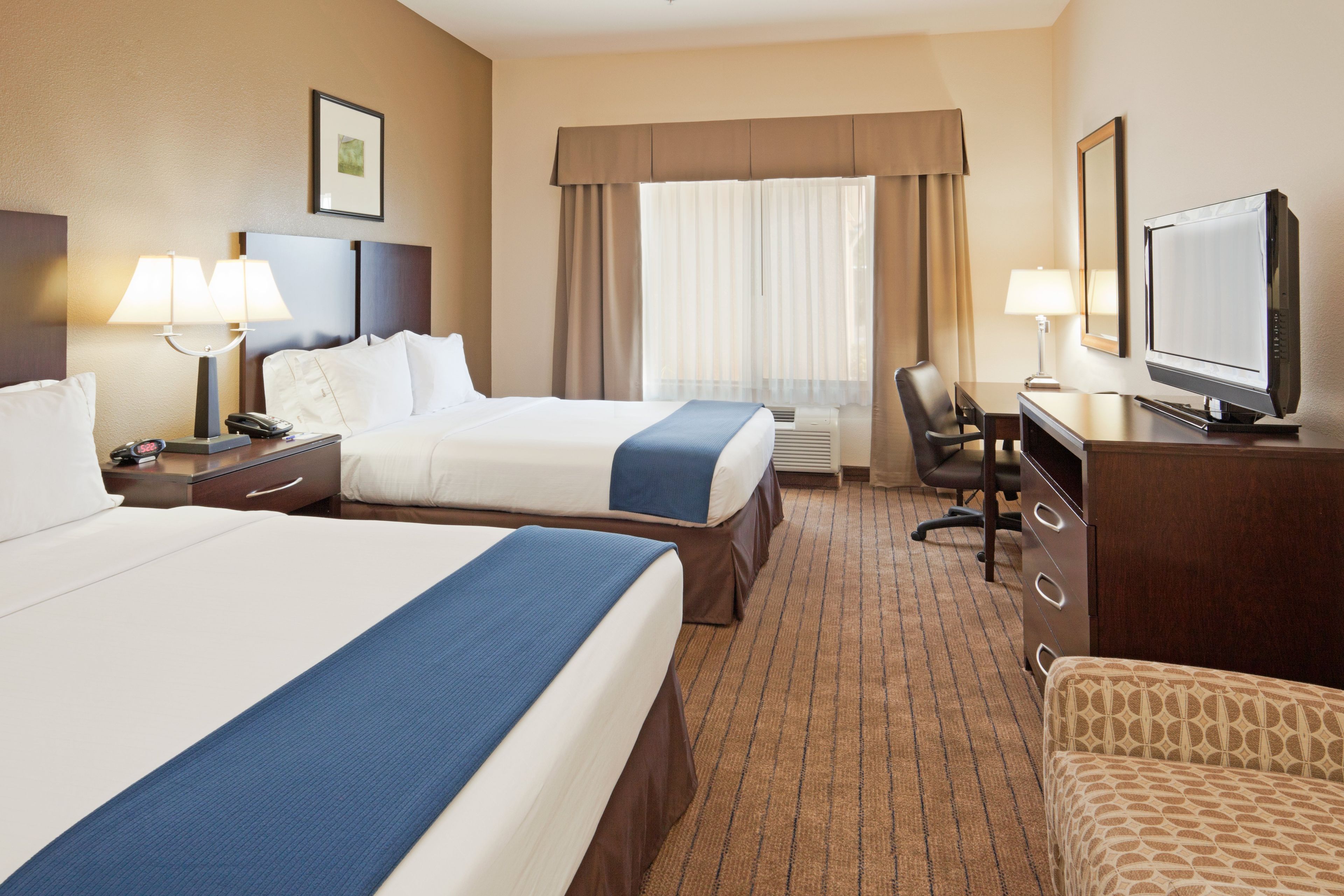 A hotel room with two beds, a desk, a chair, a television, and a window with curtains.