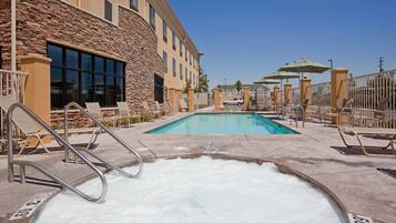 A pool area with lounge chairs and a hot tub, surrounded by a stone building with large windows.