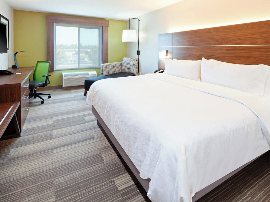 A hotel room with a large bed, a desk with a computer, a chair, and a TV.