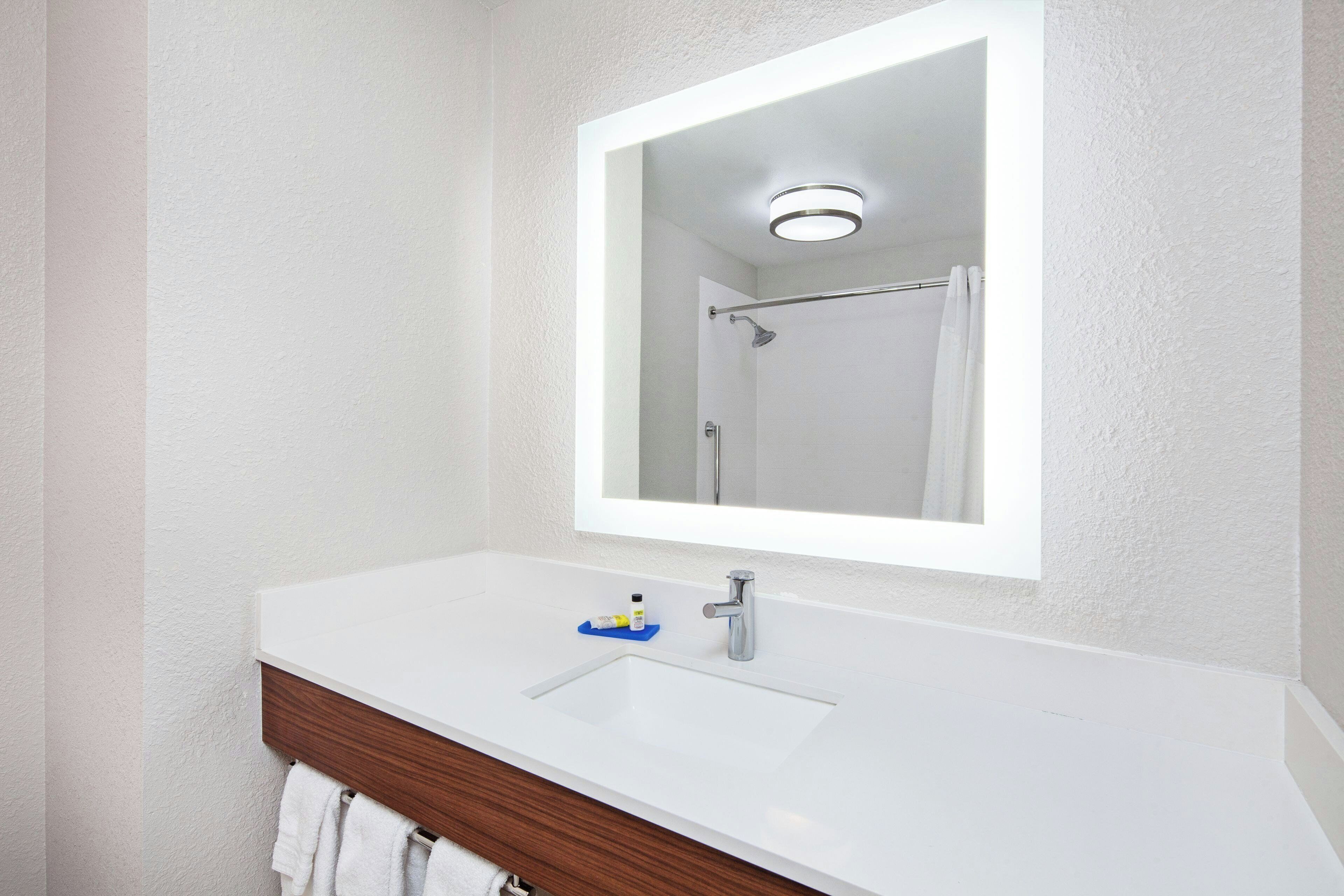 Un baño con un lavamanos blanco, un espejo y una ducha visible al fondo.