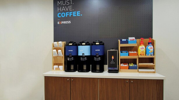 A coffee station with multiple coffee dispensers, a hot water station, and various coffee products on shelves. - Holiday Inn Express & Suites Clovis-Fresno Area by IHG (Clovis)