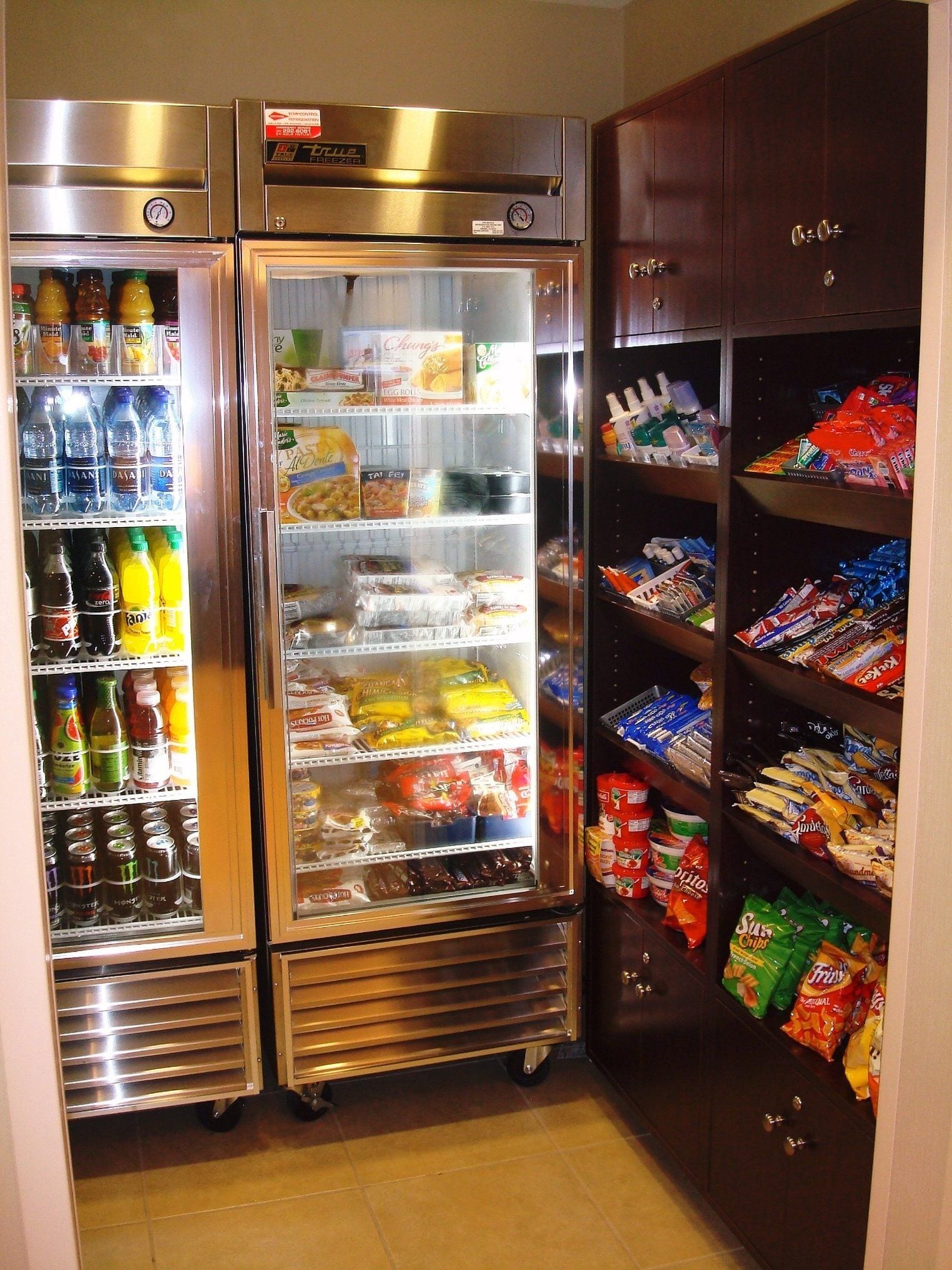 A mini-fridge stocked with beverages and snacks, a freezer with frozen goods, and a pantry with various food items.