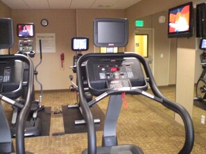 Ein Fitnessraum mit Laufbändern, Fernsehern und einer Wanduhr.