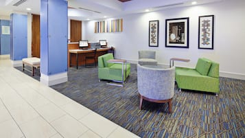 A hotel lobby with a reception desk, two computer workstations, and seating areas with green upholstered chairs.
