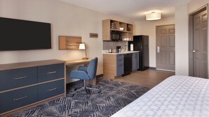 A hotel room with a bed, a desk with a chair, a kitchenette, and a TV mounted on the wall. - Candlewood Suites Springfield North by IHG (Springfield)