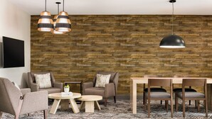 A modern living room with a brick wall, two sofas, a coffee table, a dining table with chairs, and pendant lighting. - Candlewood Suites Springfield North by IHG (Springfield)